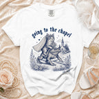 White t-shirt with blue ink graphic of cat in veil riding frog, with church, "going to the chapel" text.