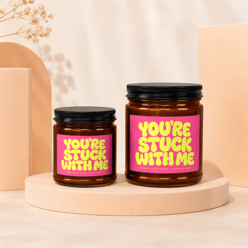 Two amber glass candles with pink labels reading "YOU'RE STUCK WITH ME" are displayed.