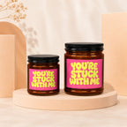 Two amber glass candles with pink labels reading "YOU'RE STUCK WITH ME" are displayed.
