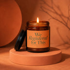 Amber jar candle with lid off, lit flame, and label reading "We Registered for This."