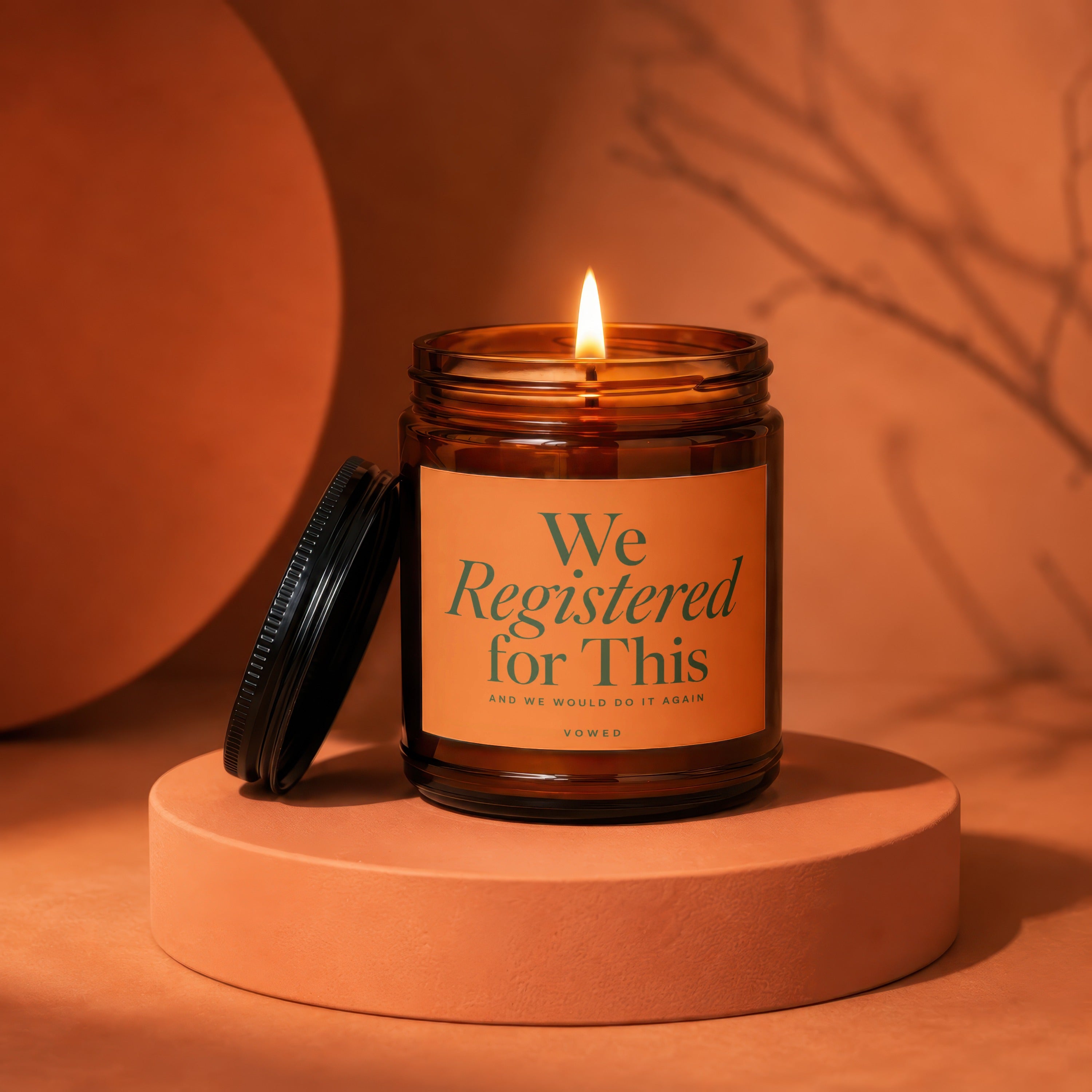 Amber jar candle with lid off, lit flame, and label reading "We Registered for This."