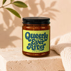Amber candle jar with black lid, yellow label reads "Queerly Ever After VOWED".
