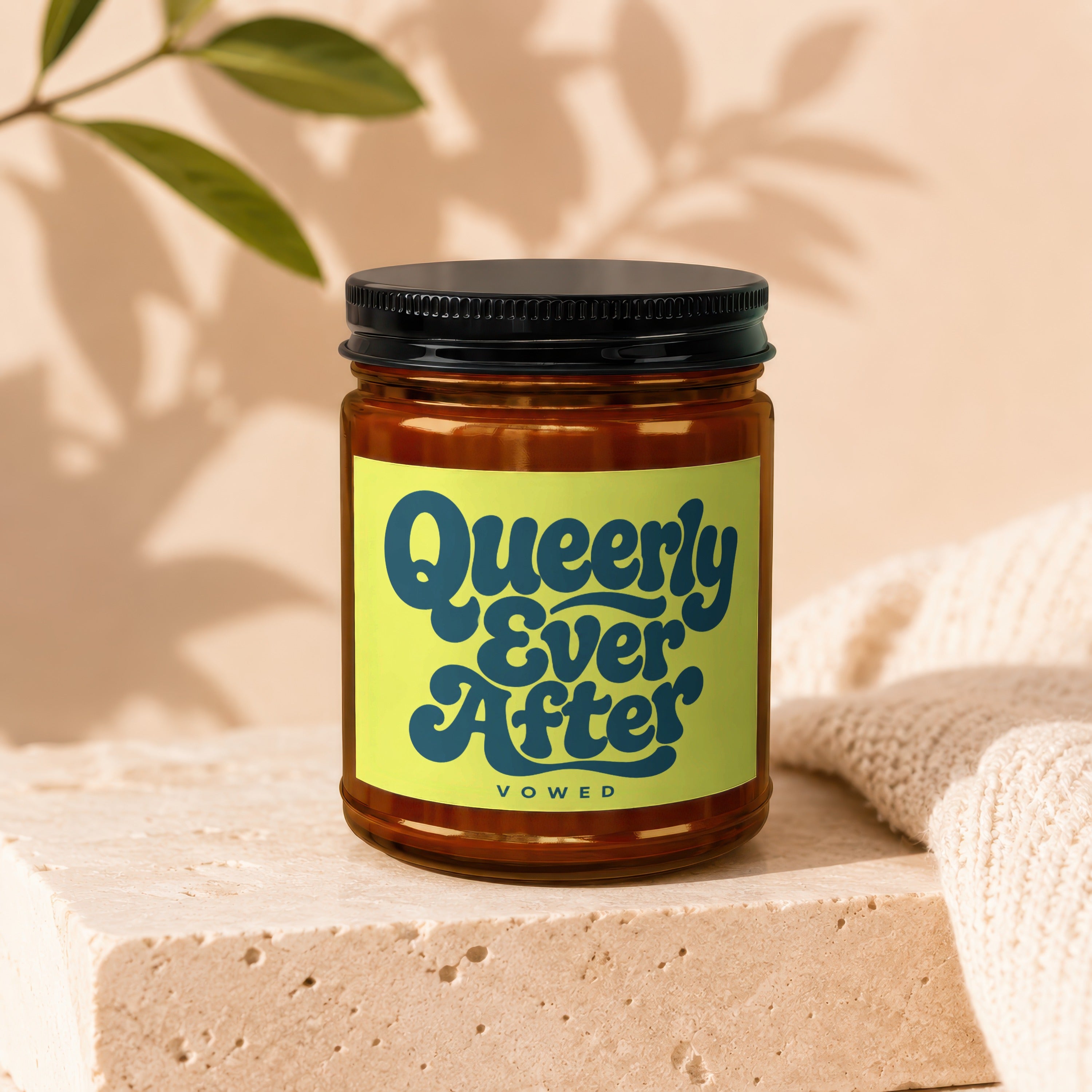 Amber candle jar with black lid, yellow label reads "Queerly Ever After VOWED".