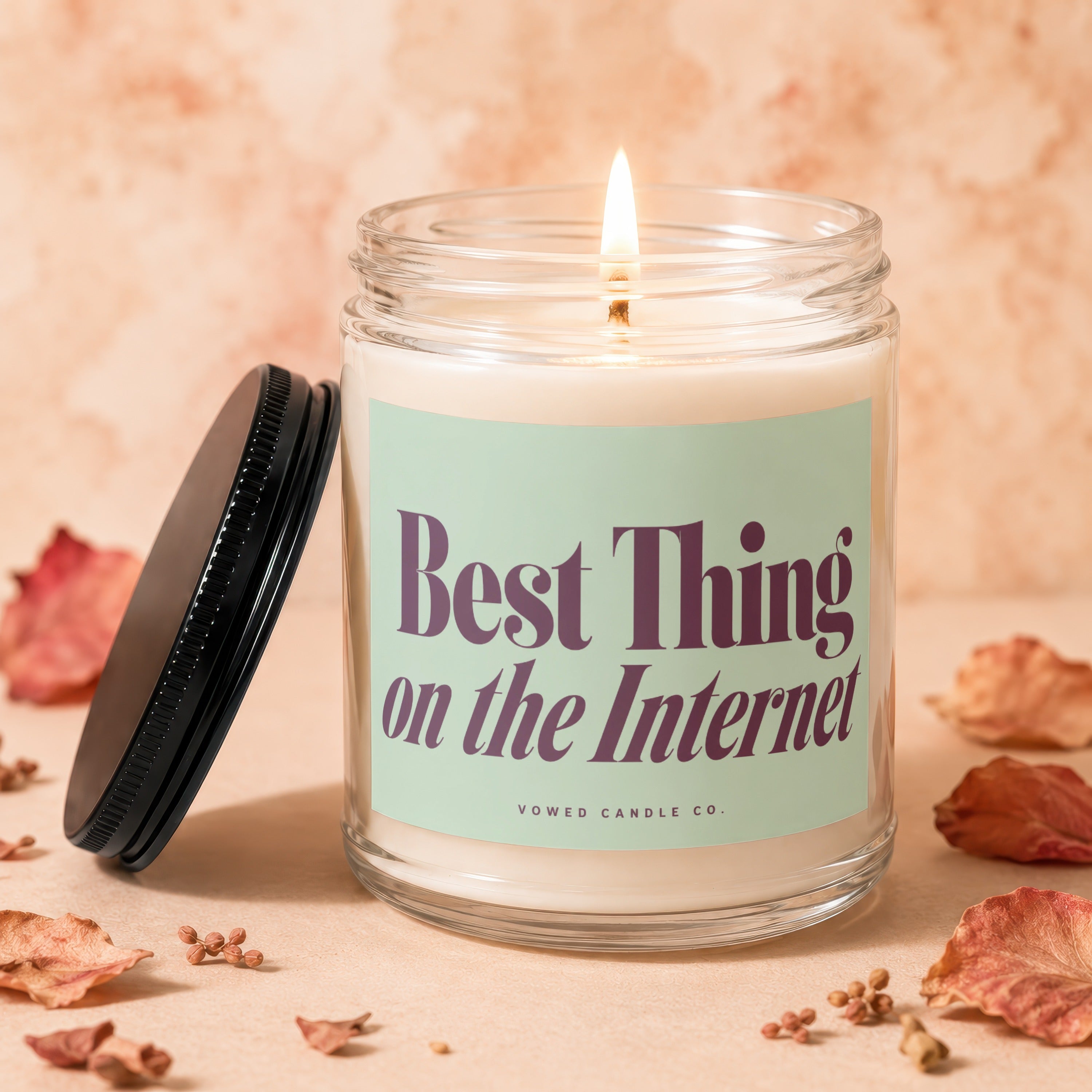 Candle with "Best Thing on the Internet" text, lit flame, and black lid.
