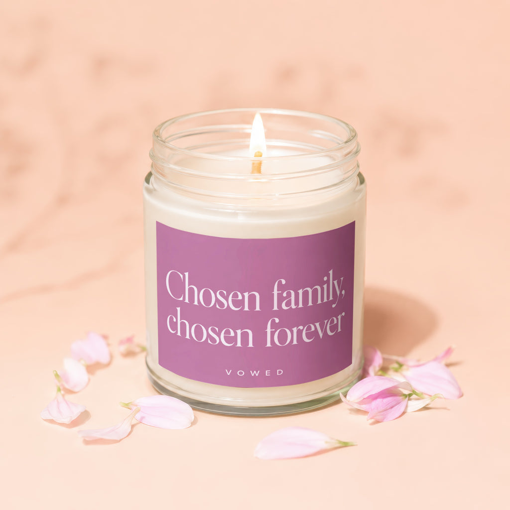 Lit candle in glass jar with purple label reading "Chosen family, chosen forever."