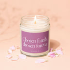 Lit candle in glass jar with purple label reading "Chosen family, chosen forever."