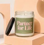Glass candle labeled "Partner for Life VOWED" with black lid propped open.