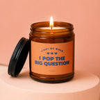 Amber jar candle with lit wick and black lid. Text reads "Light me when I pop the big question".
