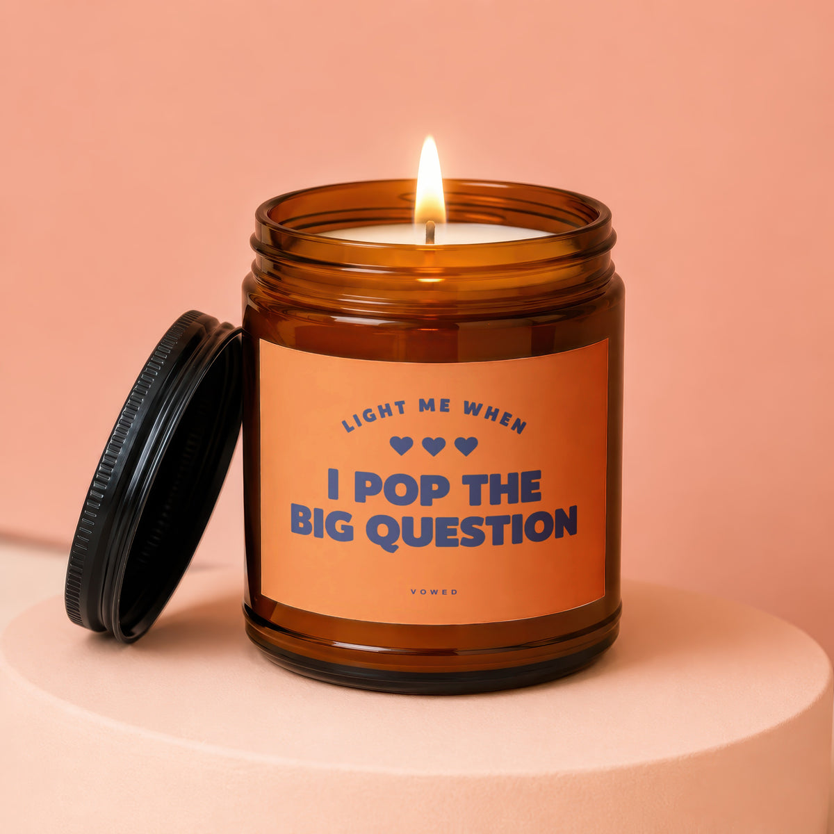 Amber jar candle with lit wick and black lid. Text reads "Light me when I pop the big question".