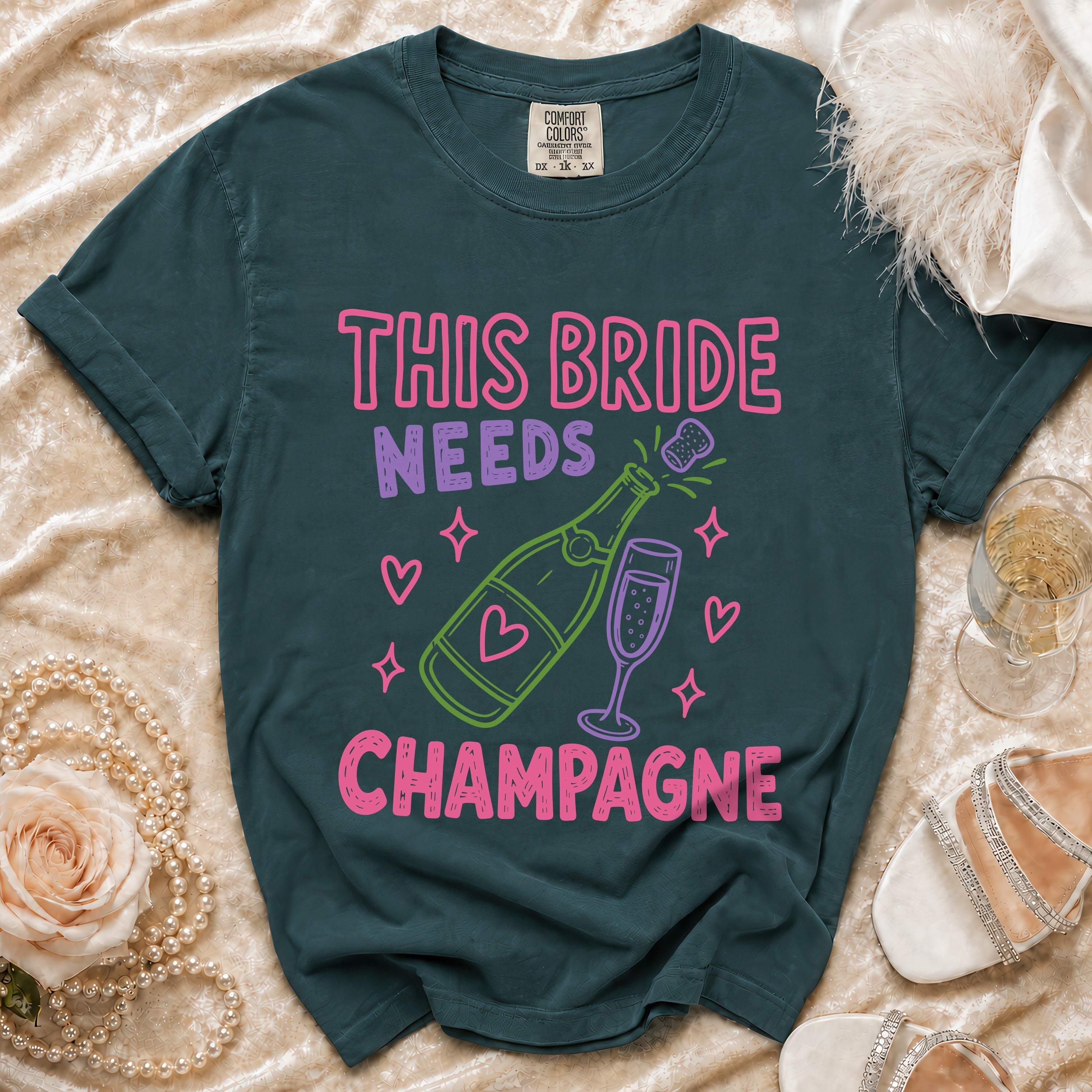 Teal t-shirt with "This Bride Needs Champagne" text and champagne bottle graphic.