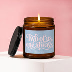 Amber glass candle with lit flame, black lid, and a label reading "Two of us, one always".