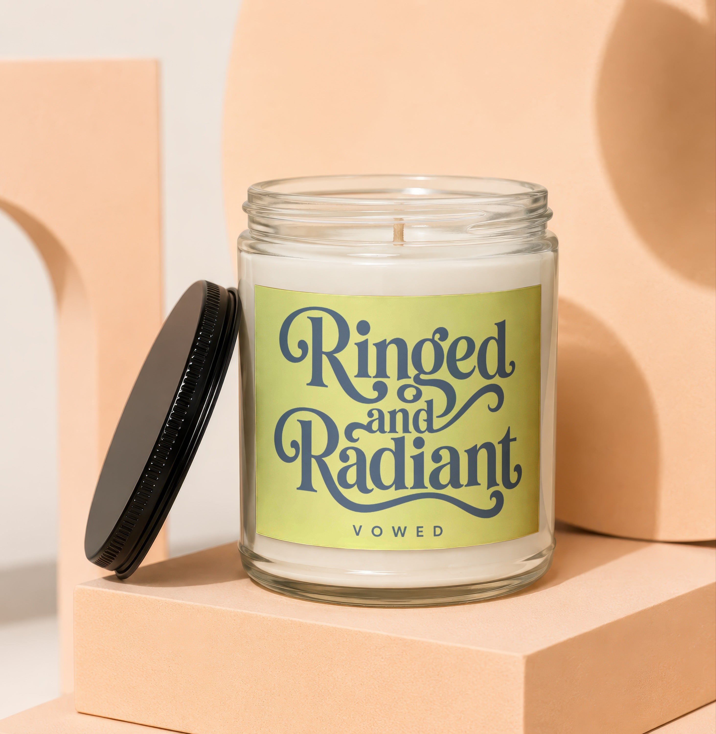 Glass jar candle with black lid and label reading "Ringed and Radiant VOWED".
