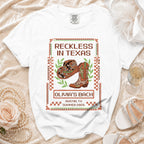 White t-shirt with "Reckless in Texas" graphic for Olivia's Bach.