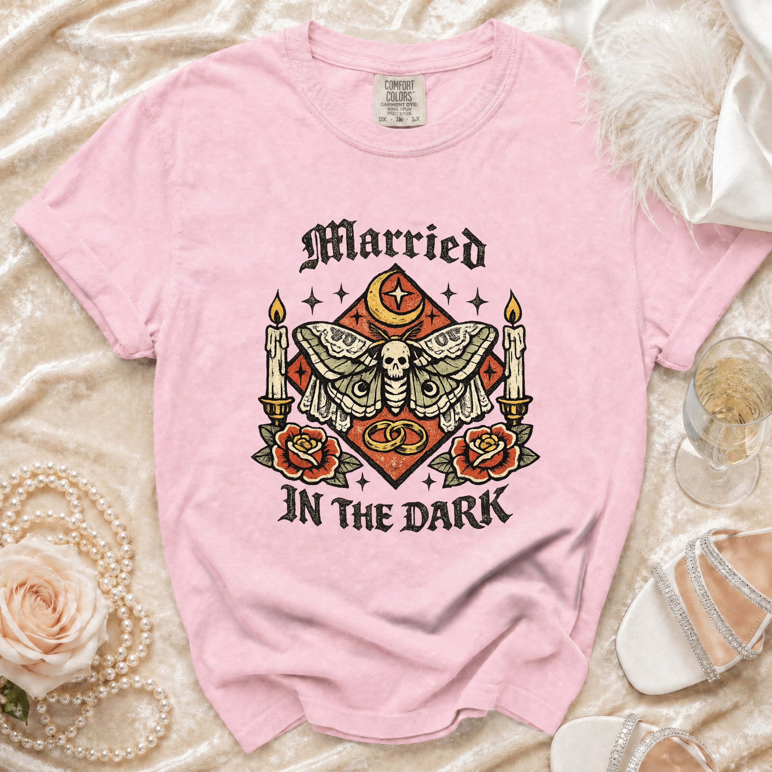 Pink t-shirt with skull, moth, candles, roses, rings saying "Married In The Dark".