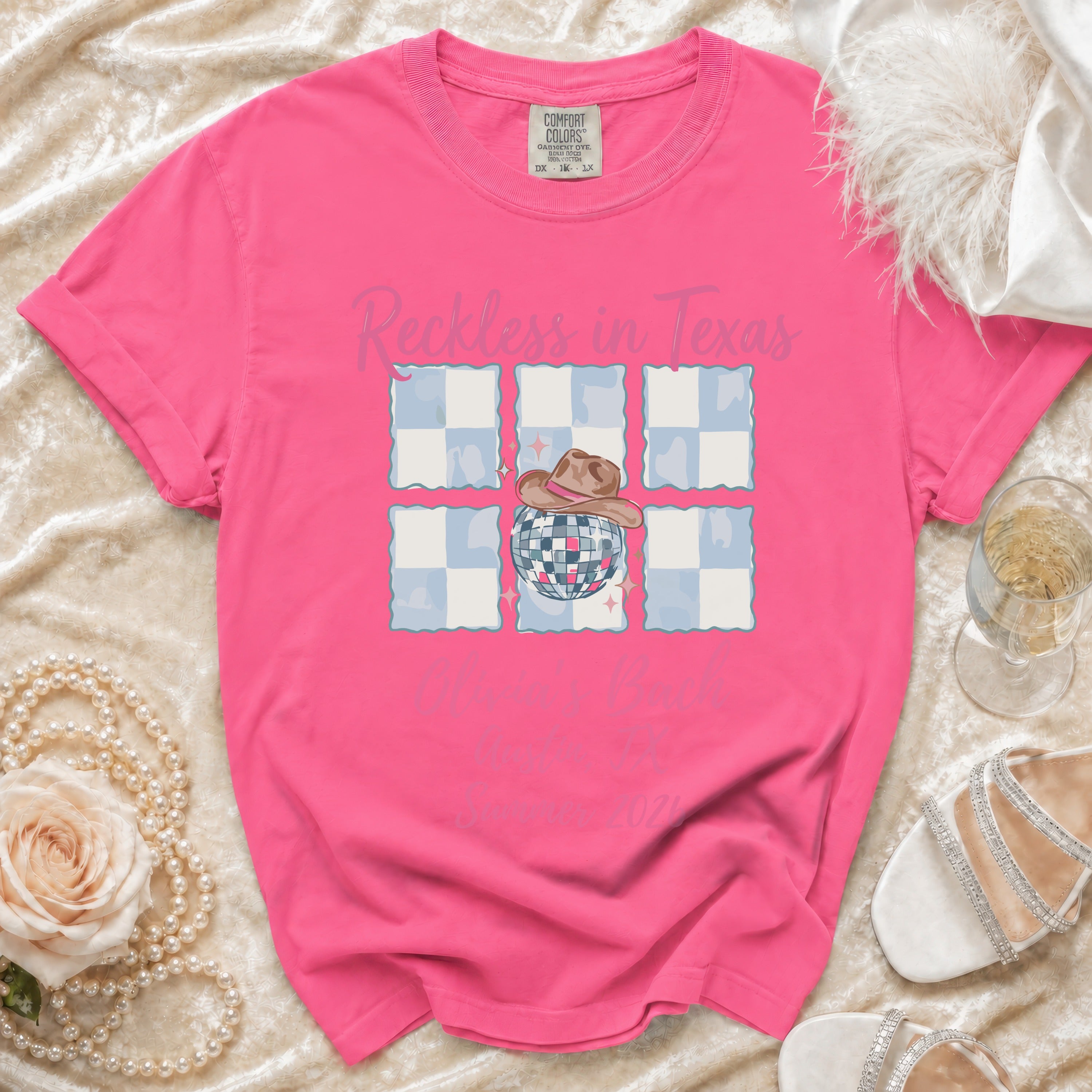 Pink t-shirt with "Reckless in Texas" text, disco ball, and cowboy hat graphic.