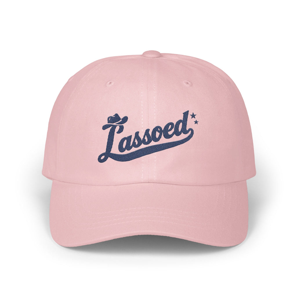 A light pink baseball cap featuring embroidered dark blue text that reads Lassoed.