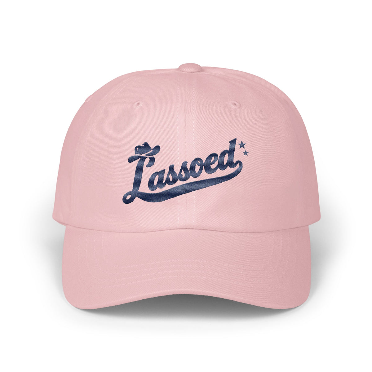 A light pink baseball cap featuring embroidered dark blue text that reads Lassoed.