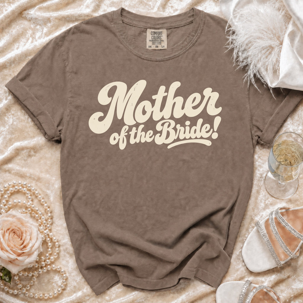 Brown t-shirt with "Mother of the Bride!" text, pearl necklace, rose, and white heels.