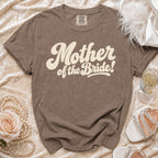 Brown t-shirt with "Mother of the Bride!" text, pearl necklace, rose, and white heels.