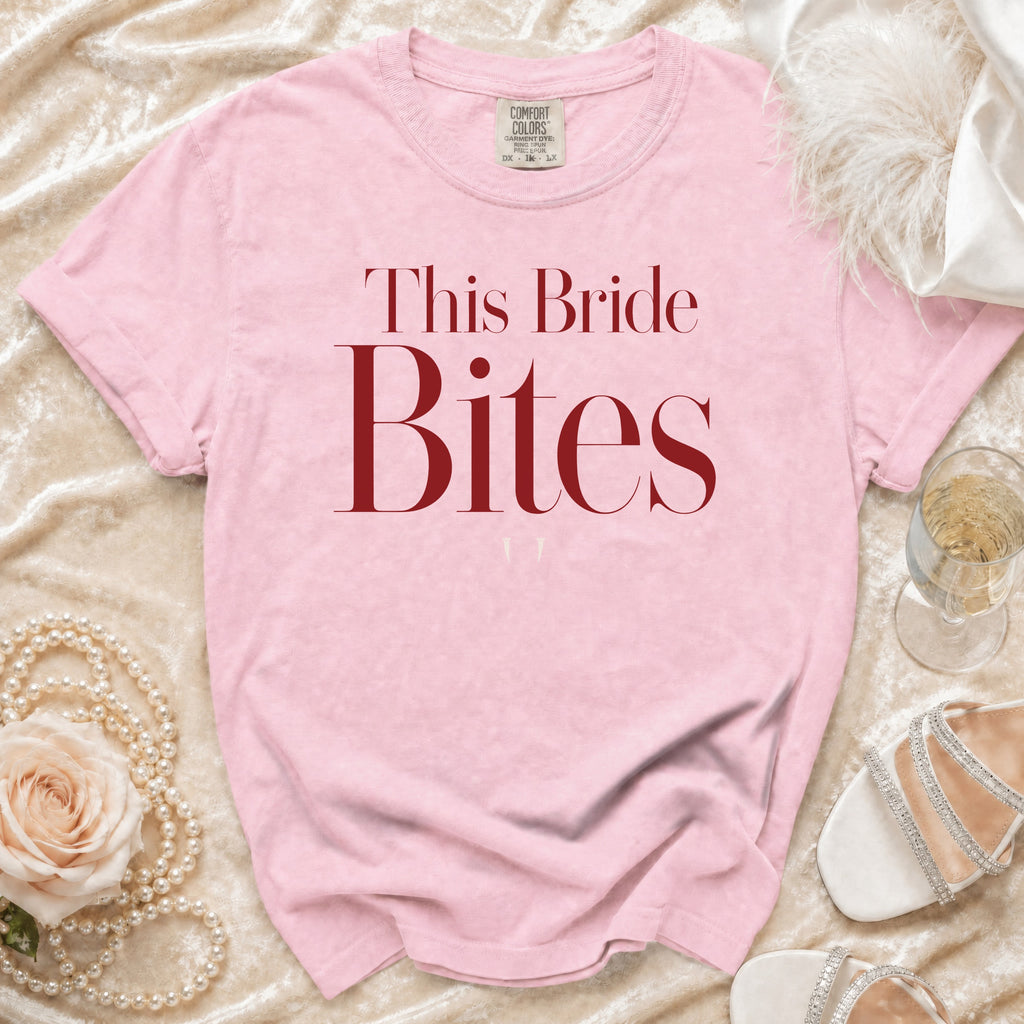Pink t-shirt with "This Bride Bites" text, displayed with pearls, rose, and shoes.