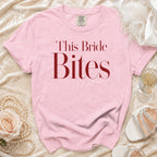 Pink t-shirt with "This Bride Bites" text, displayed with pearls, rose, and shoes.