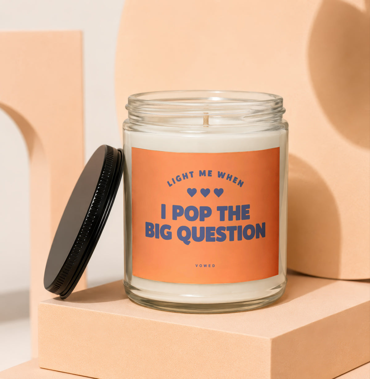 Glass candle with orange label that says "Light me when I pop the big question".
