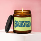 Amber jar candle with lit flame and "ENGAYGED" text on label.