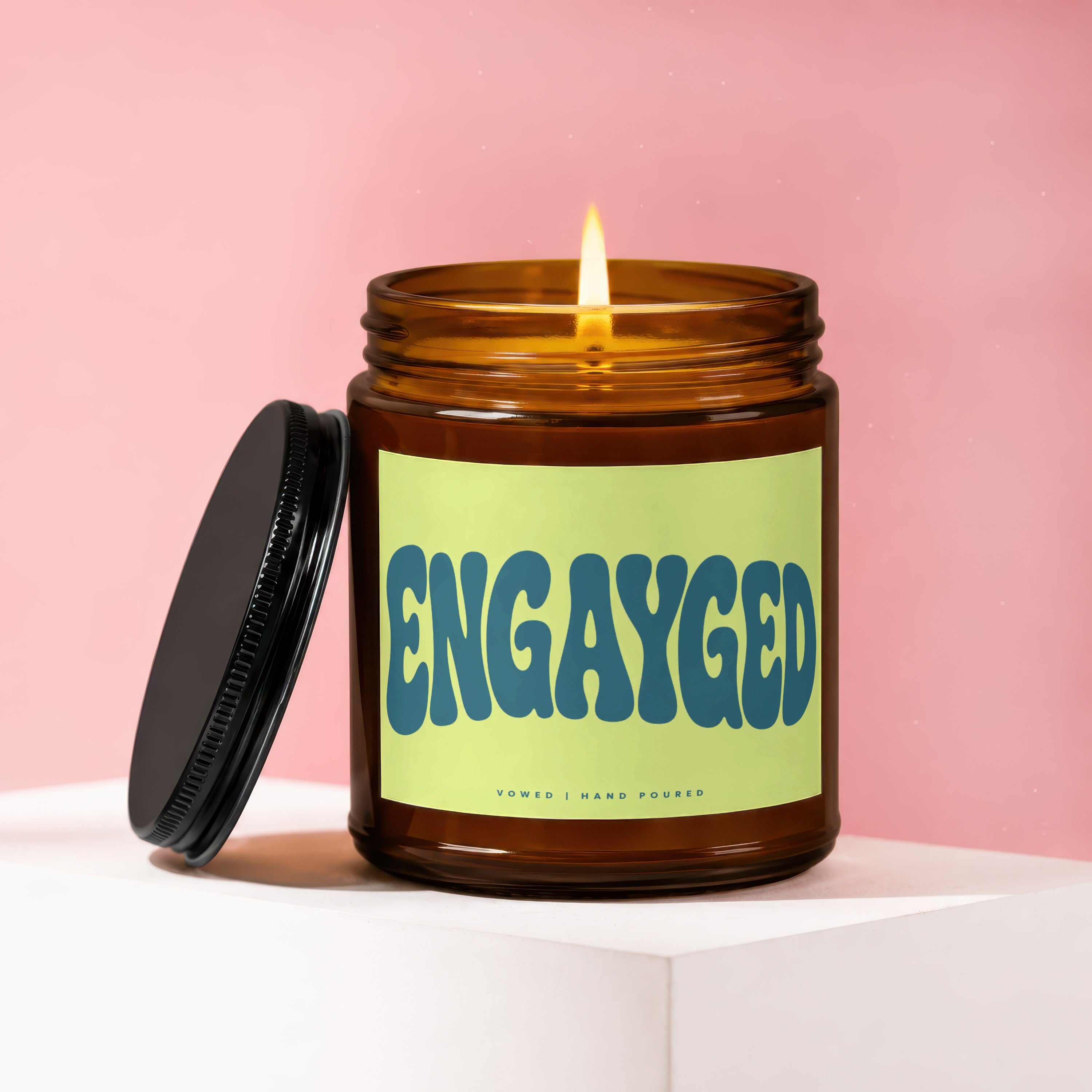 Amber jar candle with lit flame and "ENGAYGED" text on label.