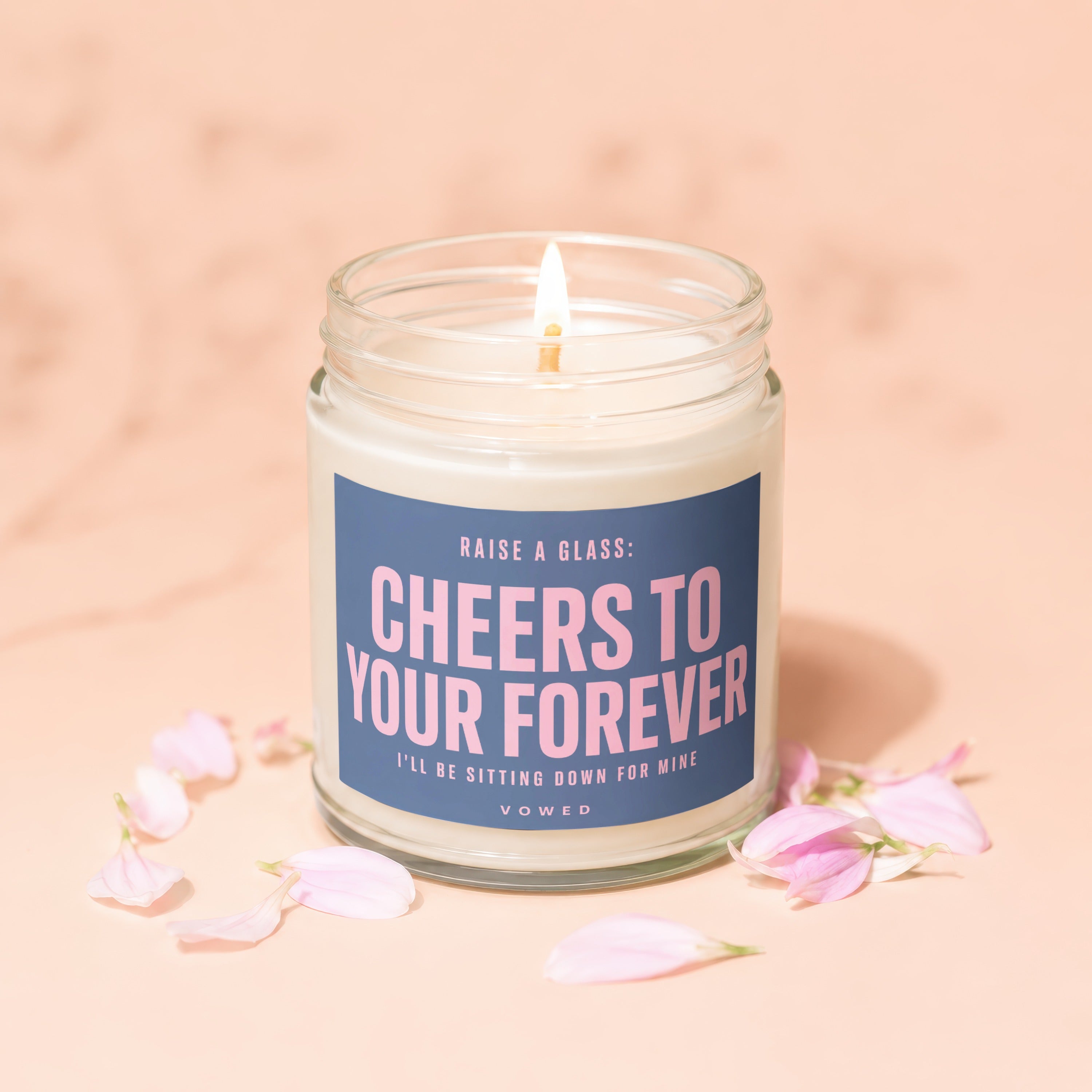Candle with label "Cheers to Your Forever" surrounded by pink flower petals.