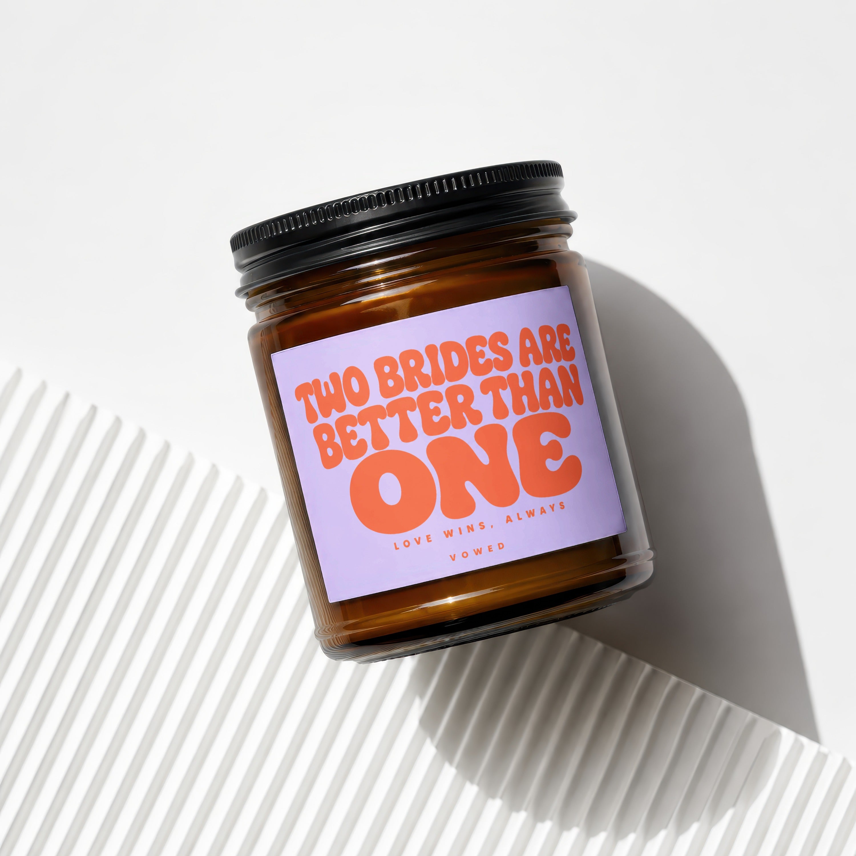 Amber jar candle with purple label reading "Two brides are better than one."