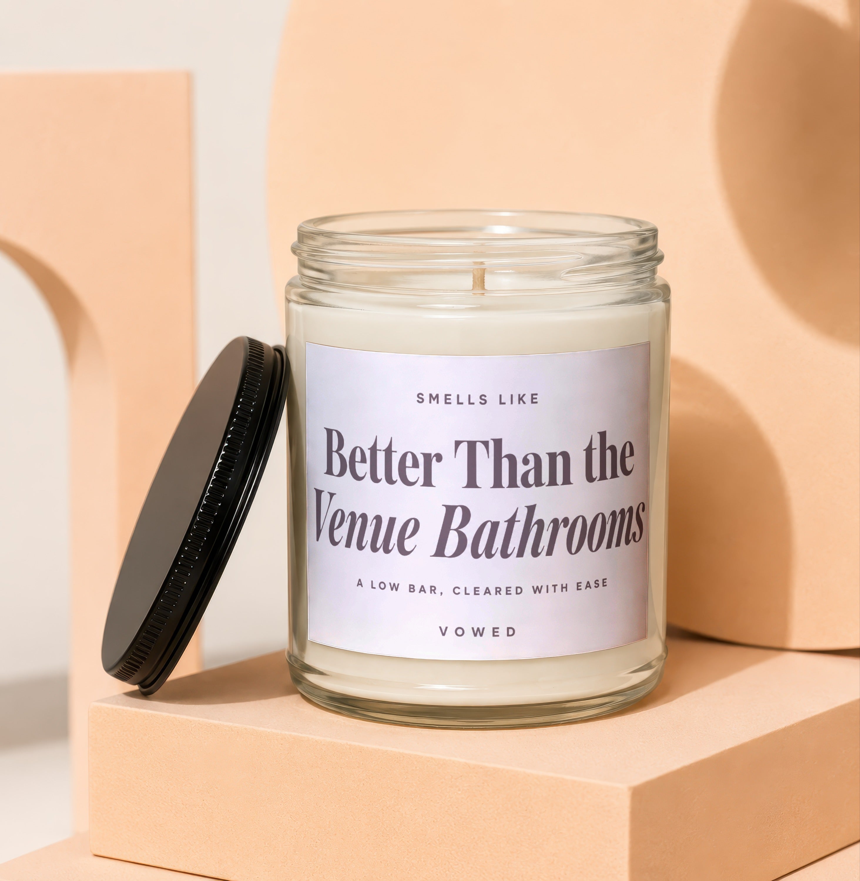Clear glass candle with black lid reads "Smells like Better Than the Venue Bathrooms. Vowed."