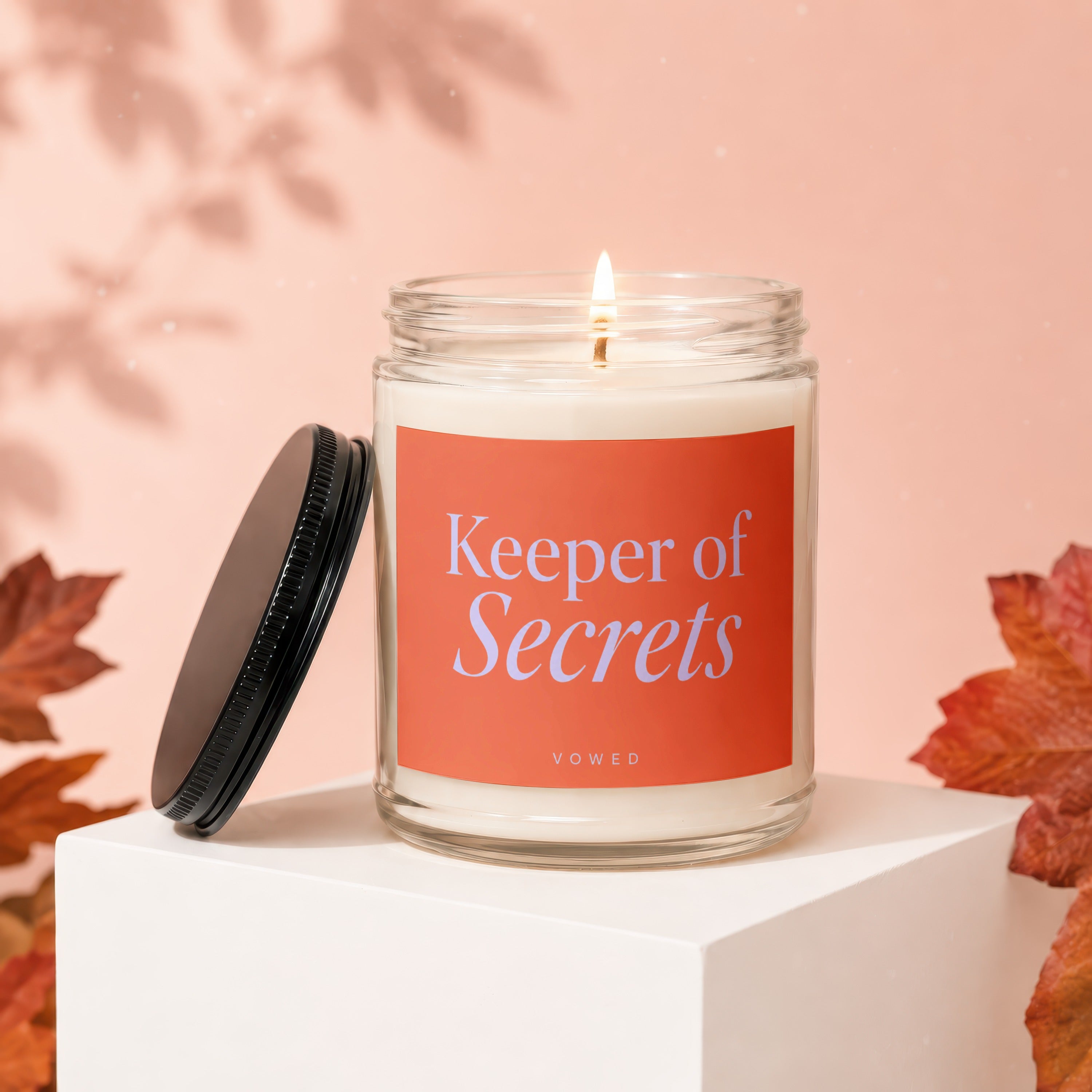 Glass jar candle with lit wick, orange label reads "Keeper of Secrets Vowed".