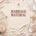 Beige t-shirt with "MARRIAGE MATERIAL" text, pearl necklace, rose, champagne, and heels.