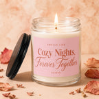 Glass jar candle with pink label reading "Smells Like Cozy Nights, Forever Together Vowed".
