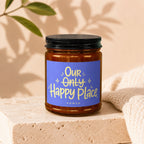 Amber jar candle with blue label reading "Our Only Happy Place VOWED".