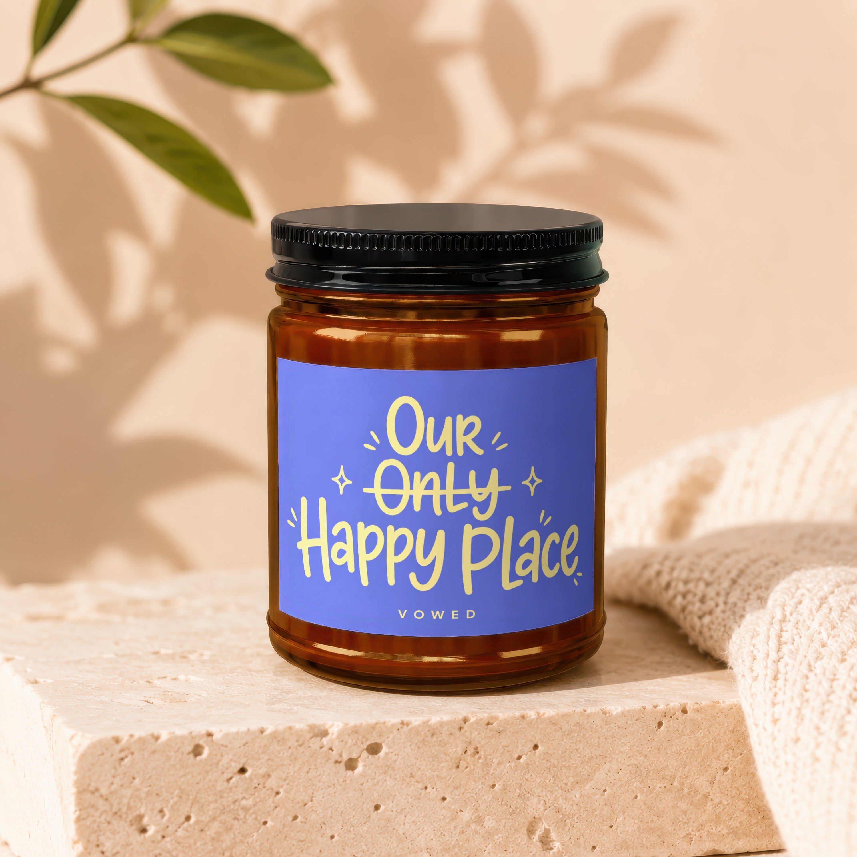 Amber jar candle with blue label reading "Our Only Happy Place VOWED".