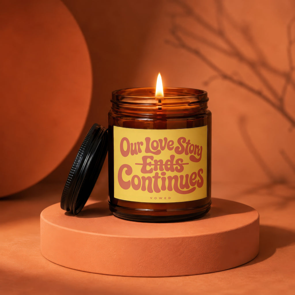 Amber jar candle with lit flame and label reading "Our Love Story Ends Continues Vowed."