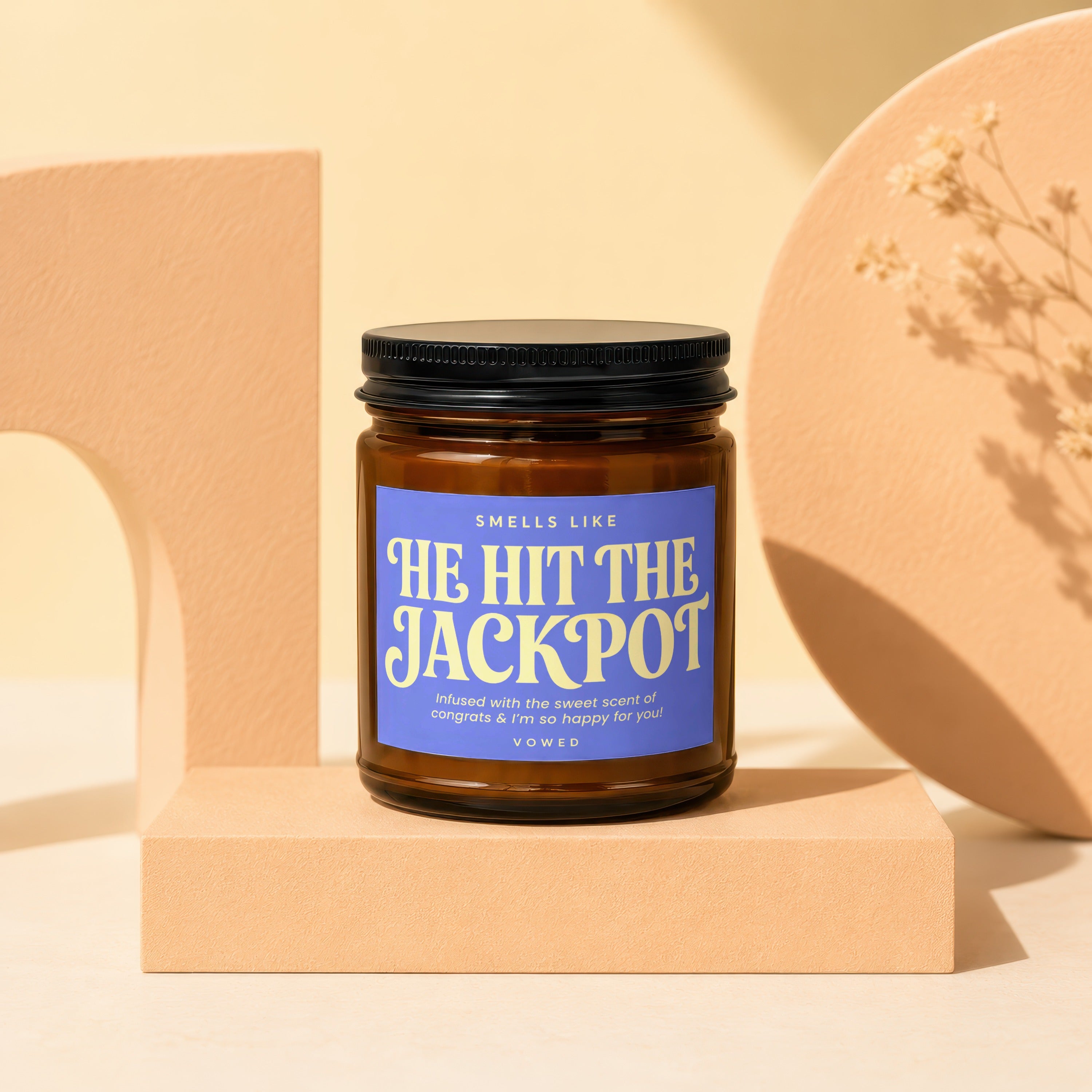 Amber jar candle with blue label reading "HE HIT THE JACKPOT."