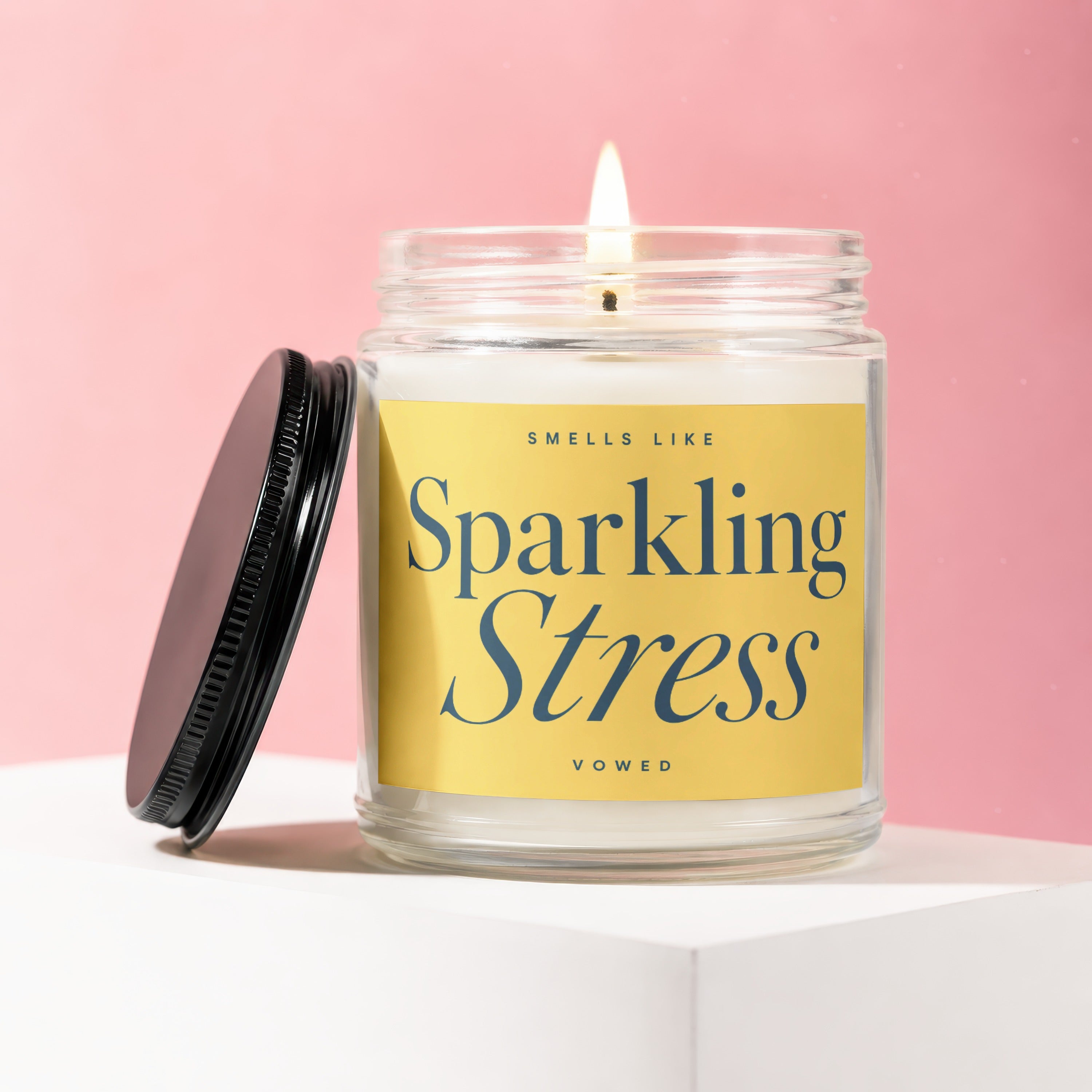 Lidded glass candle with yellow label reading "Smells Like Sparkling Stress Vowed".