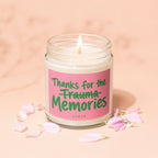 A lit candle with pink label reading "Thanks for the Trauma Memories," surrounded by pink petals.