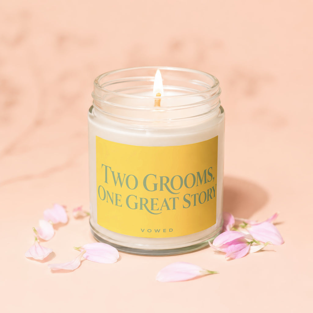 Jar candle with lit wick and yellow label that reads "TWO GROOMS, ONE GREAT STORY VOWED".