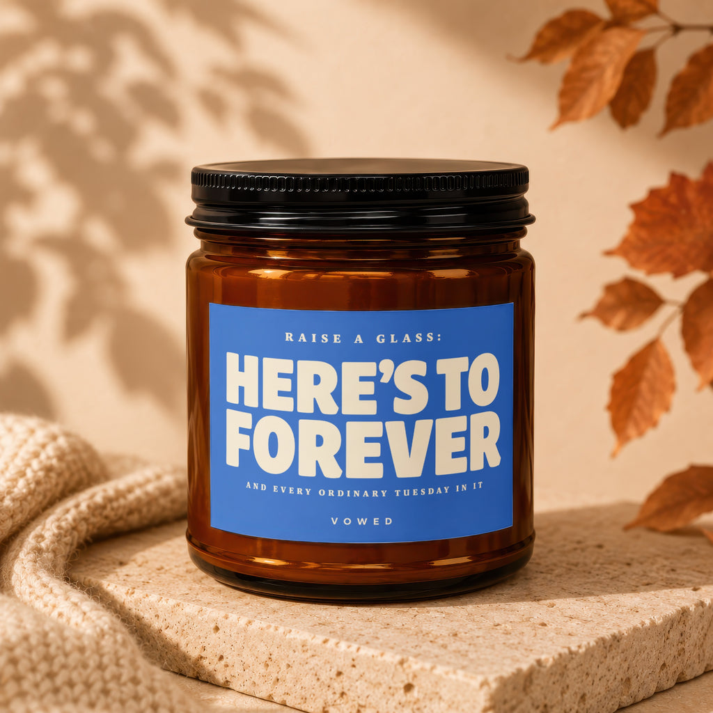 Amber candle with blue label reading "HERE'S TO FOREVER" and "VOWED."