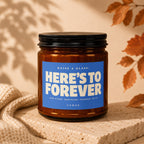 Amber candle with blue label reading "HERE'S TO FOREVER" and "VOWED."