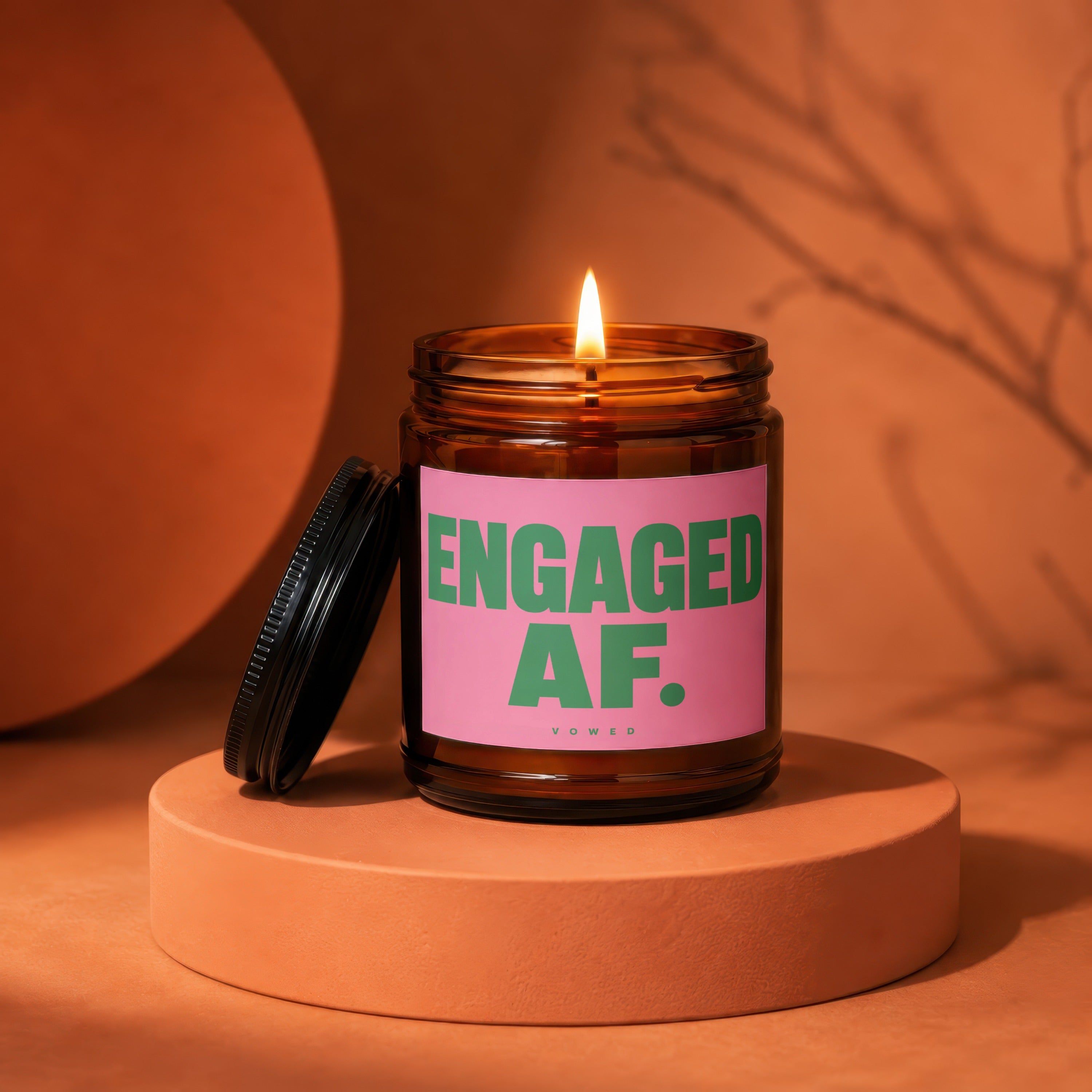 Amber jar candle with pink label reading "ENGAGED AF. VOWED".