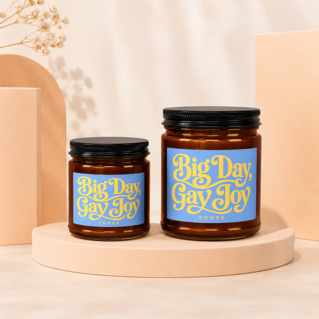 Two amber glass candles with blue labels reading "Big Day, Gay Joy" Vowed.