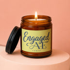 Amber jar candle with a lit wick and a yellow label reading "Engaged AF VOWED".