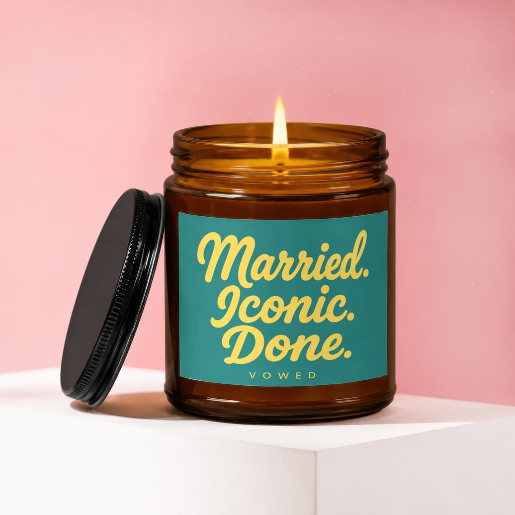 Amber jar candle with lit flame, lid to the side, reads "Married. Iconic. Done."