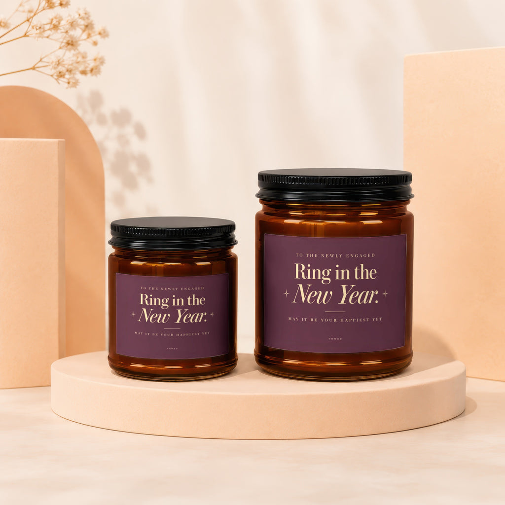 Two amber glass candles with purple labels reading "Ring in the New Year. May it be your happiest yet."