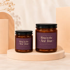 Two amber glass candles with purple labels reading "Ring in the New Year. May it be your happiest yet."