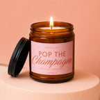 Amber jar candle with pink label that reads "Smells like Pop the Champagne She's off the market Vowed".